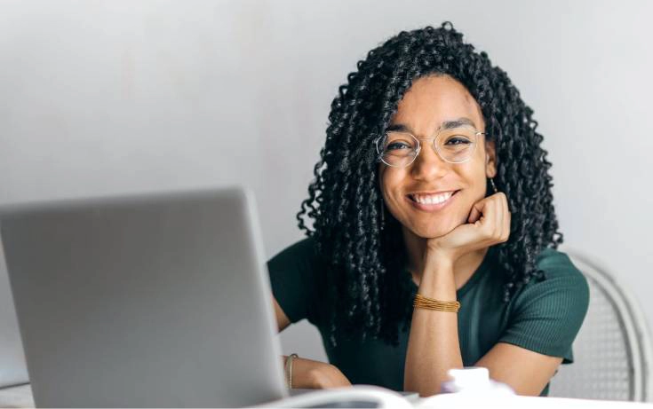 Young woman smiling at camera while using laptop